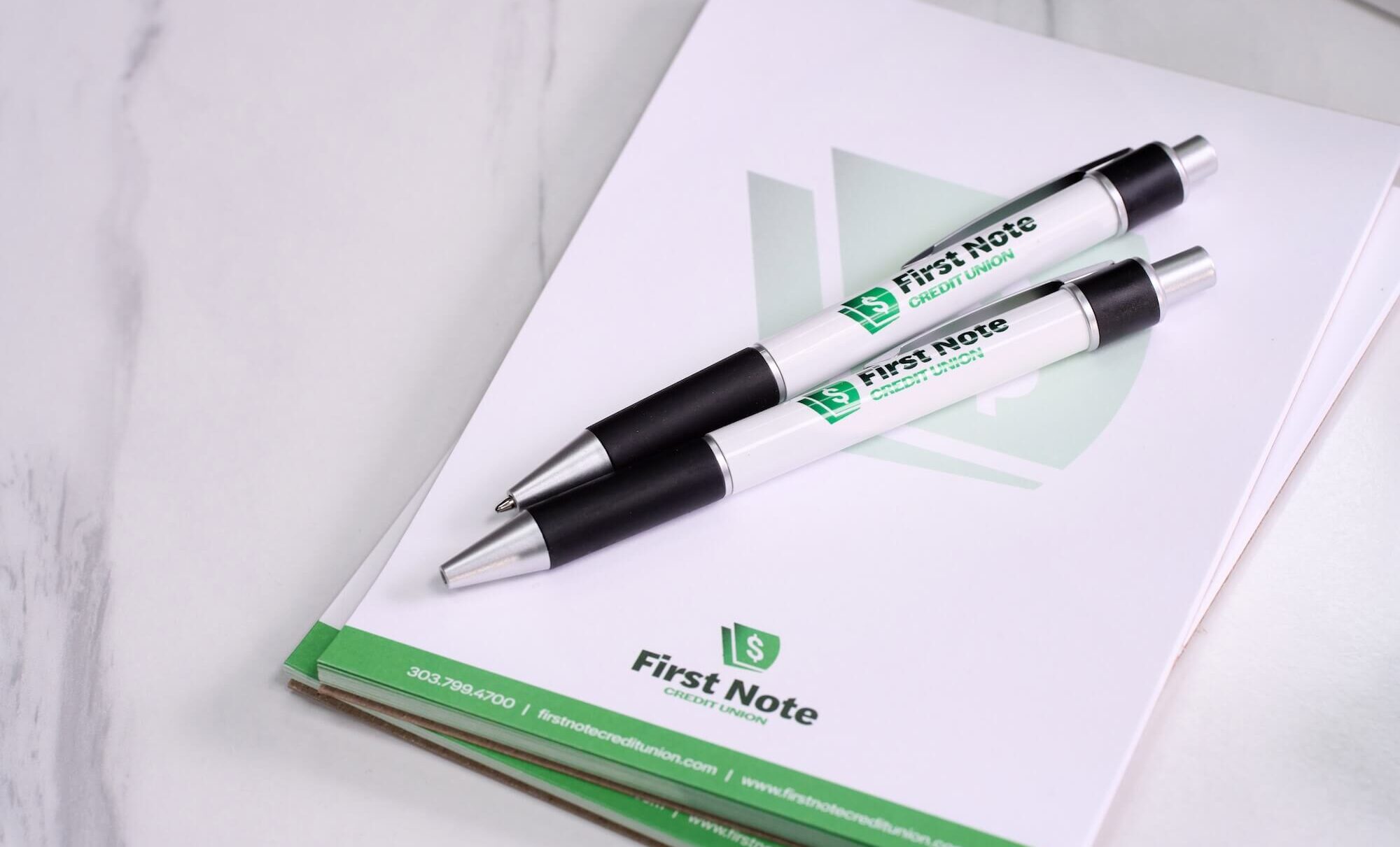 Two pens on "First Note Credit Union" branded notepad with contact details