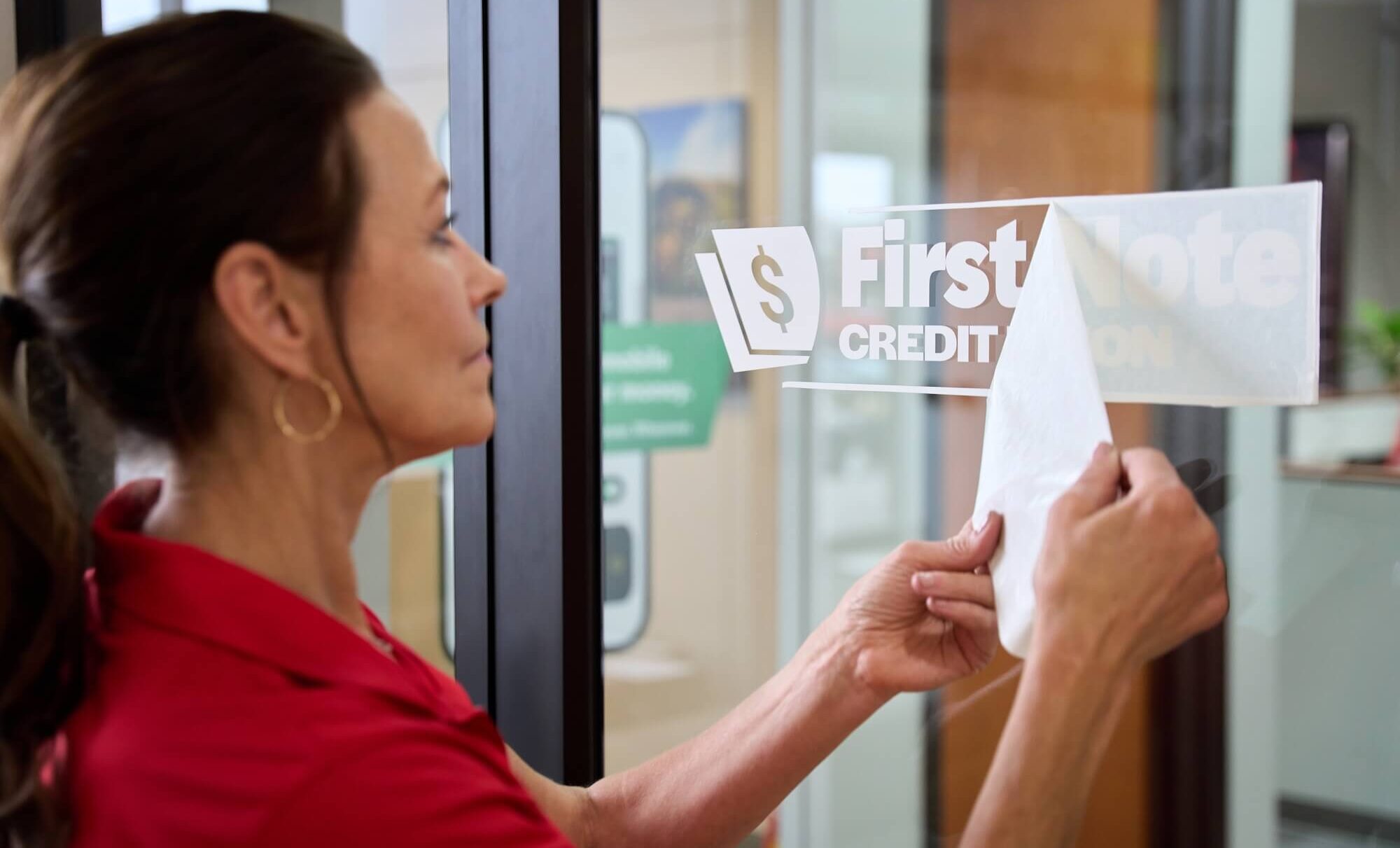 Woman applies "First Note Credit Union" sticker on glass door
