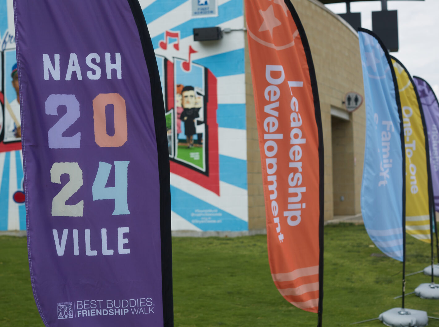 Colorful flags at 2024 Best Buddies Friendship Walk, displaying messages like "Leadership Development" and "One-To-One."